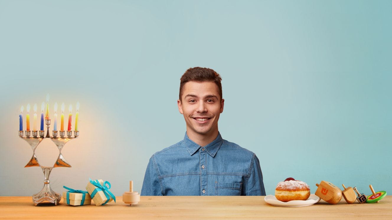 Person sitting with menorah, dreidels and doughnut against blue background
