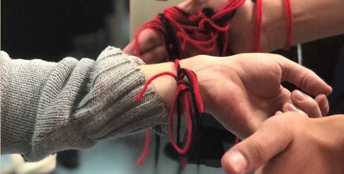 Hands with red and black yarn tied around wrists